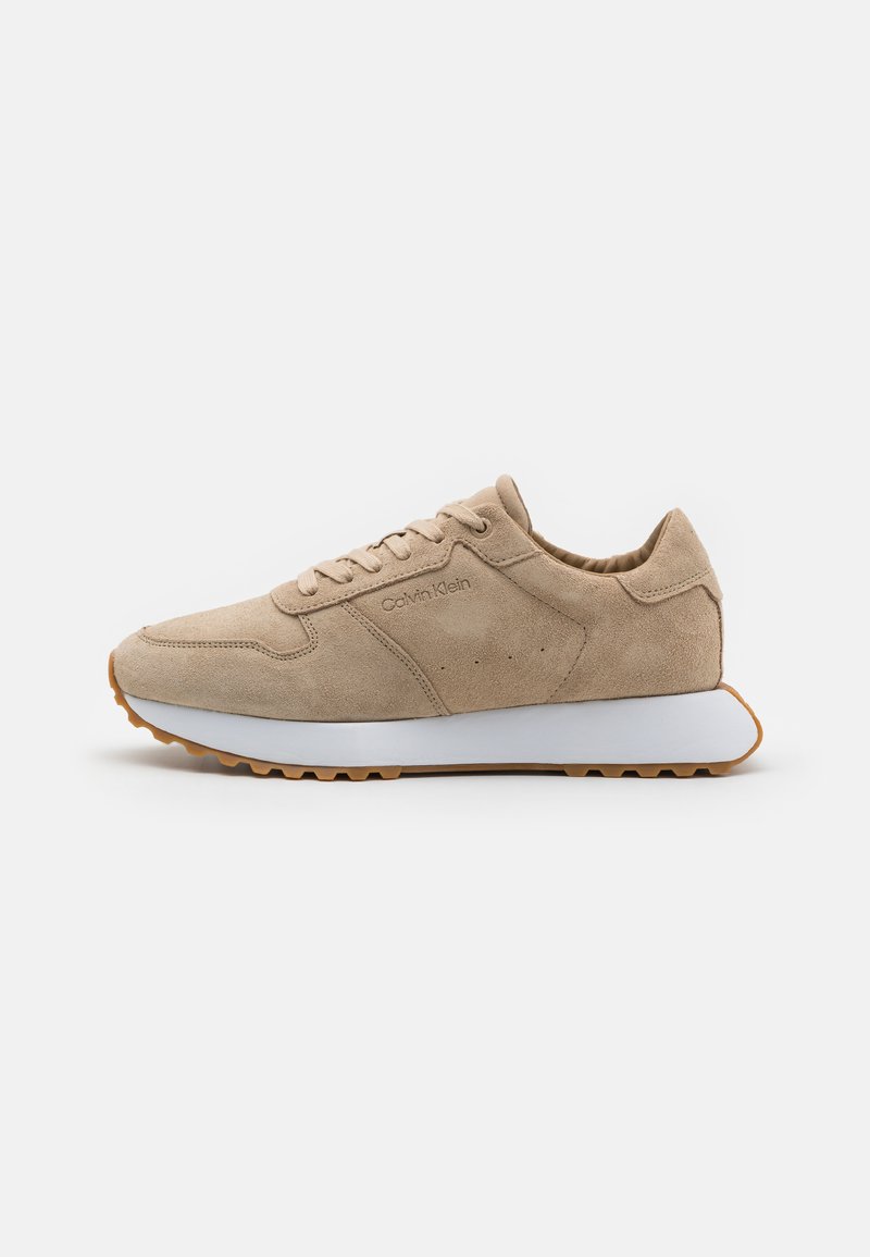 Beige mokkasiner med en hvid gummisål, rund tå og tonede snørebånd. Har brandinglogo og perforeringer for åndbarhed.