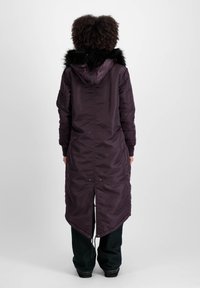 Duga ljubičasta parka s kapuljačom od umjetnog krzna, džepovima sa zatvaračem i asimetričnom donjom bordu. Glatka, izolirana tkanina s vezicom u struku.