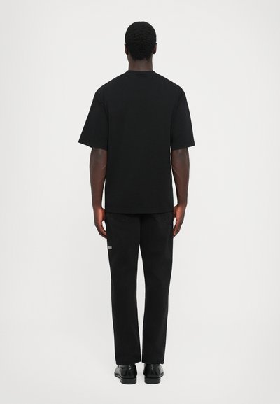 T-shirt en coton noir à manches courtes, associé à un pantalon en denim noir. La tenue a une coupe décontractée et peu d'embellissements.