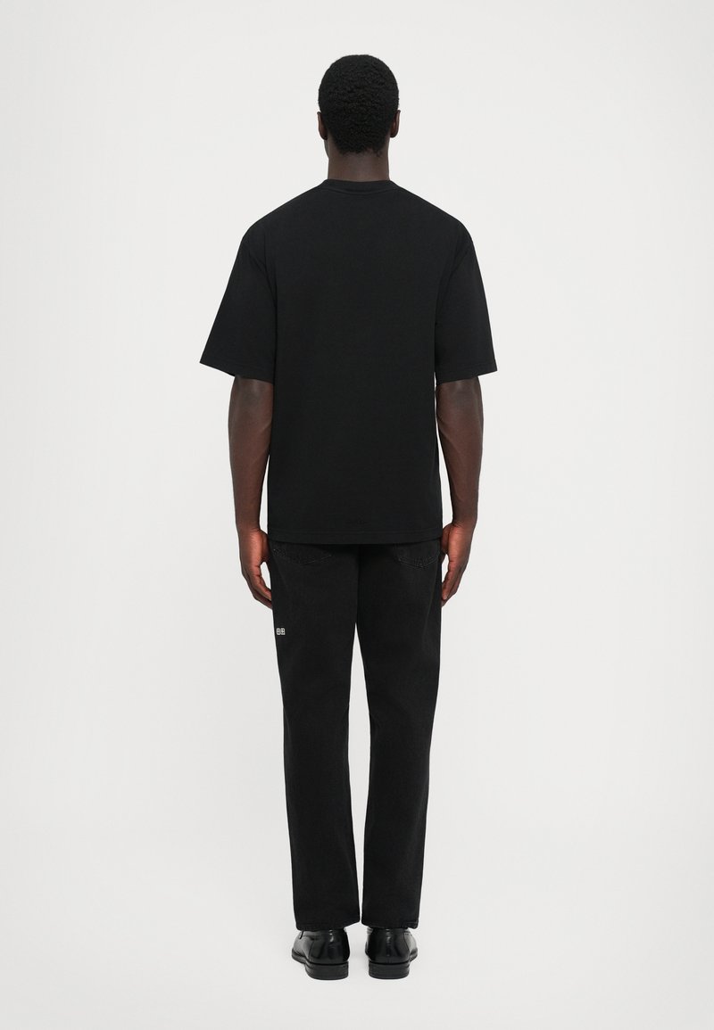 Black cotton t-shirt with short sleeves, paired with black denim pants. The outfit has a relaxed fit and minimal embellishments.