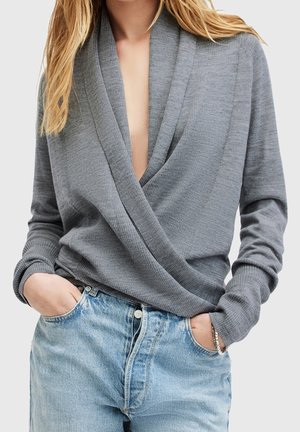 Pull en gris à col en V profond, à manches longues et texture côtelée, associé à un jean en denim bleu clair.