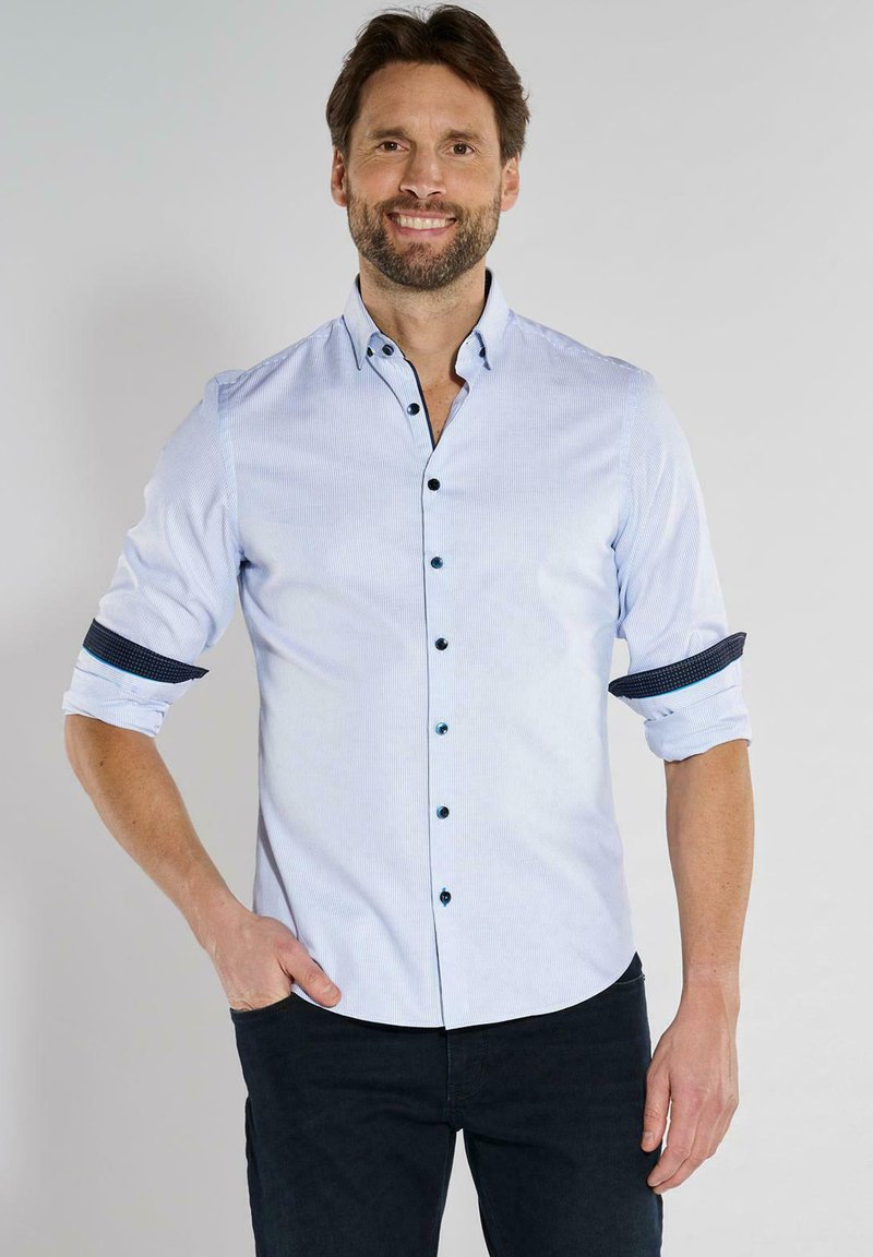 Hellblau gestreifte Hemd mit Knöpfen in Dunkel, hochgekrempelten Ärmeln und einem navy-farbenen Musterakzent, kombiniert mit dunklen Hosen.