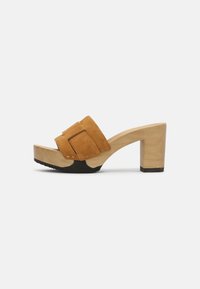 Bruine suède platform mules met een brede gesp, houten hak en gestructureerde zwarte rubberen zool. Gladde afwerking en gebogen ontwerp.