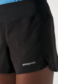 Sorte atletiske shorts med en blød tekstur, der har et logo nederst til venstre. Designet inkluderer en delt kant for øget bevægelighed.