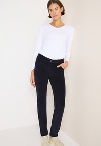 Marinblå kordbyxor med slim fit, som har framfickor och knappstängning, i kombination med en långärmad vit topp och ljusa sneakers.