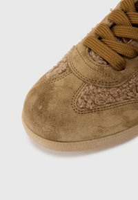 Brown suede sneaker with textured fabric accents, round toe, lace-up design, and a light rubber sole.