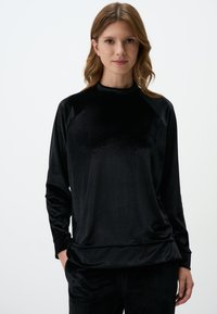 Haut en velours noir à manches longues avec un col montant, présentant une coupe décontractée et des manches raglan, mettant en valeur une texture lisse et un éclat subtil.