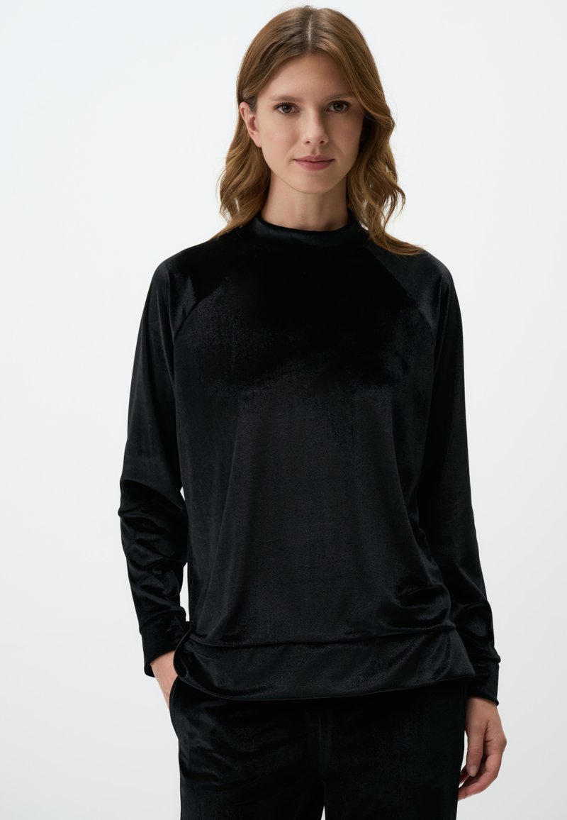 Haut en velours noir à manches longues avec un col montant, présentant une coupe décontractée et des manches raglan, mettant en valeur une texture lisse et un éclat subtil.