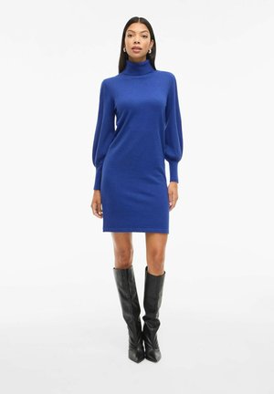 Vestido de punto azul con un escote alto, mangas globosas y una silueta ajustada, combinado con botas negras hasta la rodilla. Textura suave en todo.