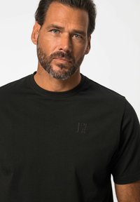 Camiseta negra de manga corta en tejido suave, con un sutil logo en relieve en el pecho y un clásico cuello redondo.