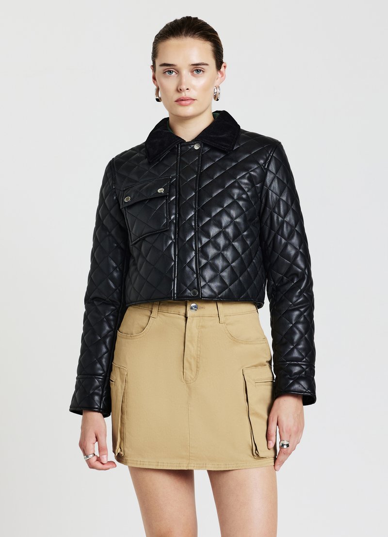 Veste en cuir matelassé noire, cropped, avec un col texturé noir et une poche frontale, associée à une mini-jupe beige avec des poches latérales.