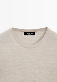 Pull beige à col rond avec texture en maille fine et étiquette noire Massimo Dutti cousue à l'intérieur du col indiquant "Fabriqué en Chine".