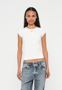 Vit figursydd t-shirt med korta ärmar, rund halsringning och en liten emblem på bröstet; kombinerad med ljusblåa denimjeans.