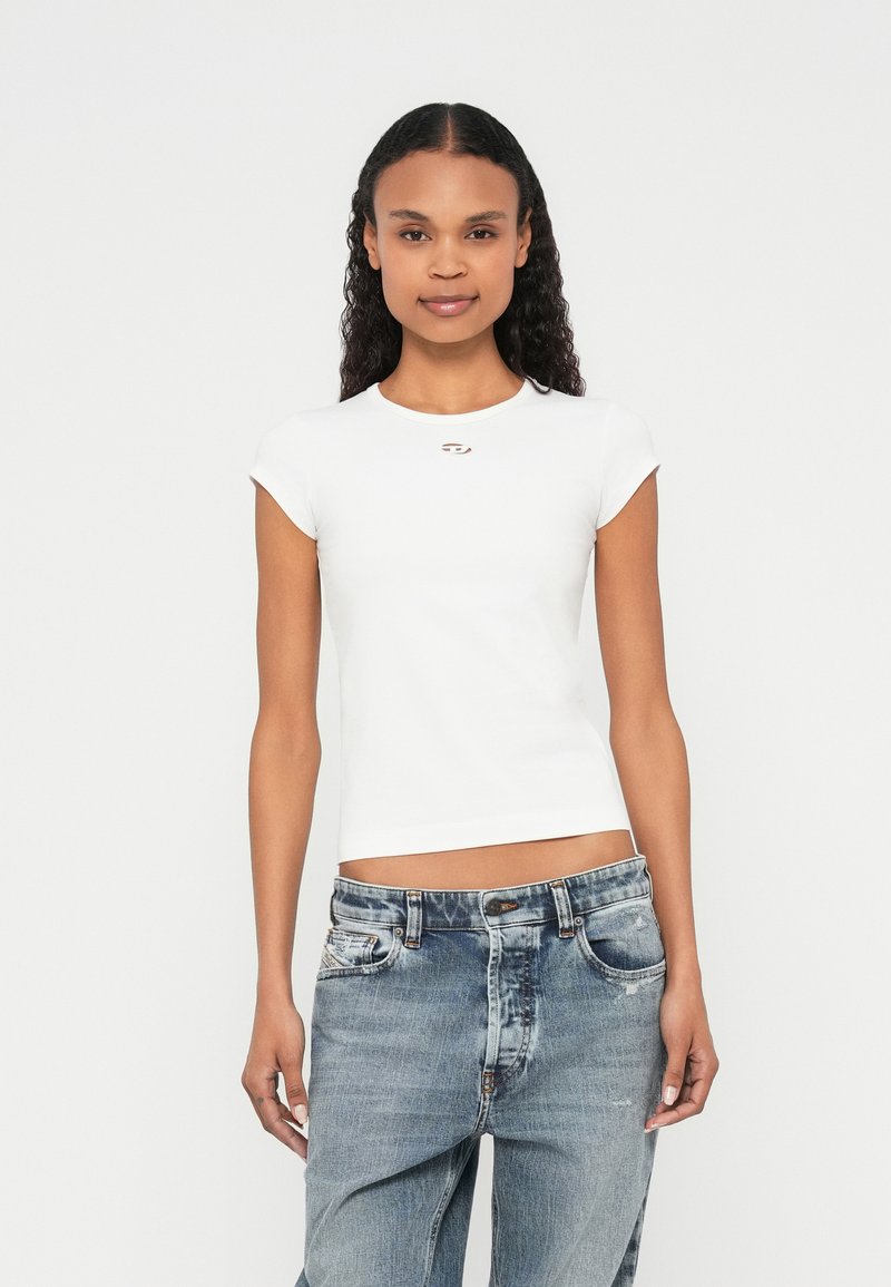 Vit figursydd t-shirt med korta ärmar, rund halsringning och en liten emblem på bröstet; kombinerad med ljusblåa denimjeans.