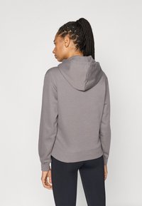 Γκρι φούτερ με κουκούλα με κορδόνι, μανσέτες και τελείωμα με ριμπ ύφανση, και απαλό, υφασμάτινο φινίρισμα. Στην πίσω πλευρά έχει έναν μίνιμαλ σχεδιασμό χωρίς διακοσμητικά στοιχεία.