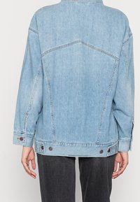 Ljusblå jeansjacka med avslappnad passform, som har två knappar vid ärmslut och distinkta detaljer vid ryggen.