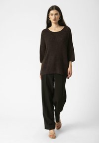 Pull en tricot marron foncé avec un large décolleté et des manches trois quarts, associé à un pantalon noir loose et des sandales beiges.