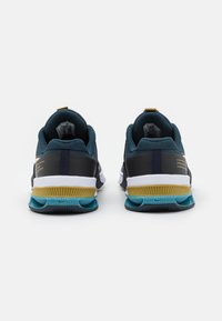 Sportskor med en mörk turkos nätövre del, vita och guldiga detaljer samt en texturerad gummisula med turkosa och grå inslag.