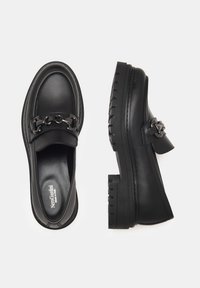 Mocassins en cuir noir avec une semelle à relief épais, présentant un accent décoratif en chaîne sur le devant et un design à bout rond.