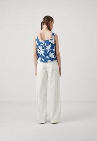 Blue floral top with white pattern, features a square back and buttons. Paired with white wide-leg trousers, smooth fabric, relaxed fit.