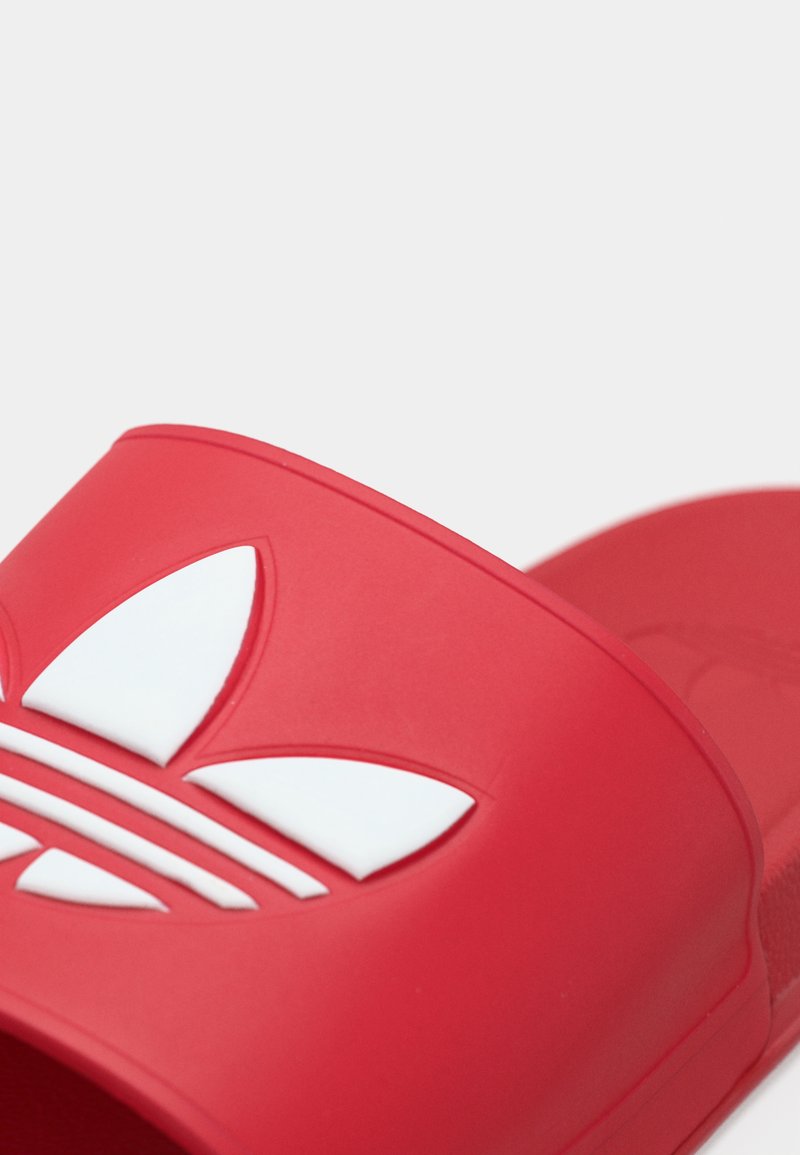 Rød gummislidesandal med bred rem, der har et hvidt logo med tre striber og et blad-design som accent. Glat tekstur, åben tå.