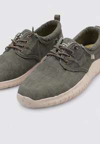 Zapatos de ante verde oscuro con puntera redondeada, suela de goma color topo, diseño de cordones y forro interno de contraste. Presentan una lengüeta en el talón.