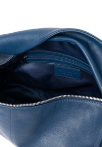 Interno di una borsa in pelle blu con una texture morbida, caratterizzato da una tasca con zip e rivestimento in tessuto. Forma arrotondata con una chiusura a zip robusta.
