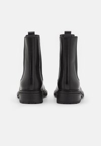 Bottes cheville en cuir noir présentant un design épuré, des panneaux latéraux élastiques et un talon épais pour la stabilité. Détails de coutures visibles.