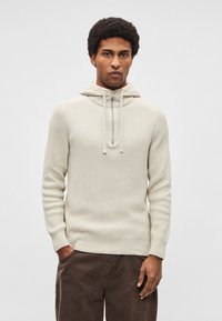 Sweatshirt com capuz em malha bege clara com tecido texturizado, gola alta e fecho de correr. Apresenta um corte descontraído e mangas compridas. Combina com calças castanhas.