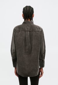 Pelēka kordurojas krekls ar aizmugurējo krokumu un pogām aizdares aprocēm, ar brīvu piegriezumu un klasisku apkakli. Gluda tekstūra visā krekla virsmā.