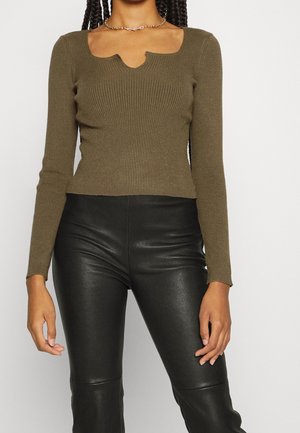 Olive ribbed long-sleeve top with a unique scalloped neckline, paired with high-waisted black faux leather pants.
