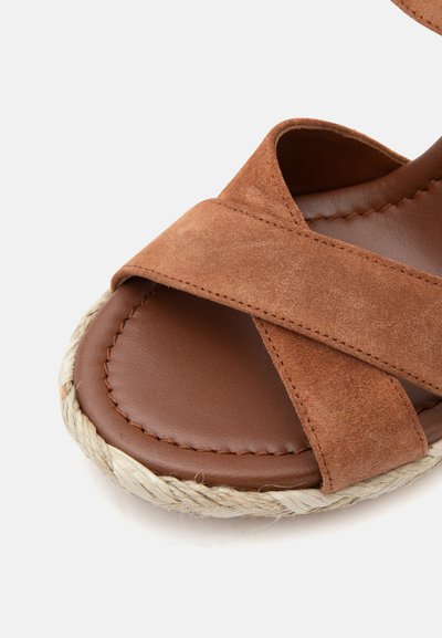 Sandale en daim marron avec de larges brides croisées et une semelle intérieure en cuir cousue, avec un bord de semelle en jute tressée.