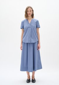 Top azzurro chiaro a maniche corte con scollo a V e dettaglio plissettato, abbinato a una gonna lunga coordinata di tonalità simile, realizzata in tessuto liscio.
