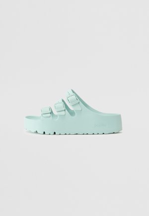 Sandalias de slip-on azul claro con tres correas ajustables, hechas de un material similar al caucho, con suelas texturizadas y logo de la marca en el lateral.