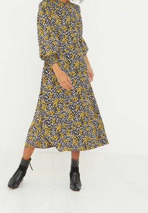 Robe noire à motifs floraux jaunes et blancs, longueur mi-mollet, manches bouffantes, encolure ronde, associée à des bottines noires.