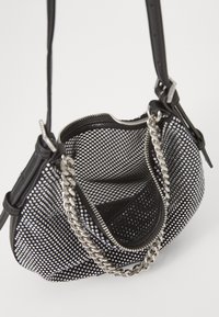 Black mesh handbag featuring silver studded detailing, a zipper closure, and a silver chain accent handle. Interior has a soft lining.
