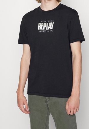 Černé tričko s krátkým rukávem s centrálním bílým logem, které říká "ORIGINAL REPLAY BLUE JEANS." Měkký bavlněný materiál s klasickým kulatým výstřihem.