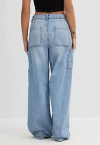 Pantalones vaqueros de pierna ancha en azul claro, con cintura alta, que presentan dos bolsillos traseros y bolsillos laterales adicionales. Tienen una textura suave y un corte relajado.