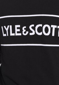 Pull noir en tricot avec le nom de la marque "LYLE & SCOTT" en lettres blanches et grasses, avec un accent horizontal blanc en dessous.