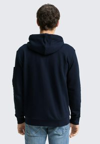 Marineblauer Hoodie aus strukturierter Fabrik, mit Kapuze und gerippten Bündchen. Verfügt über eine Seitenasche mit einem Reißverschlussdetail.