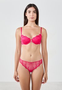 Ensemble en dentelle rouge comportant un soutien-gorge et un slip assortis, avec des bords festonnés et des motifs floraux, des sangles réglables et un détail central décoratif.