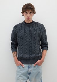Dunkelgrauer Strickpullover mit Rundhalsausschnitt und gerippten Bündchen, kombiniert mit hellblauen, verblichenen Jeans. Einfaches Design, strukturierter Stoff.