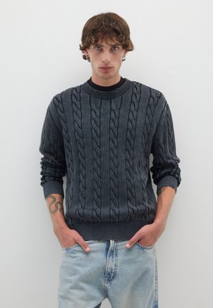 Dunkelgrauer Strickpullover mit Rundhalsausschnitt und gerippten Bündchen, kombiniert mit hellblauen, verblichenen Jeans. Einfaches Design, strukturierter Stoff.