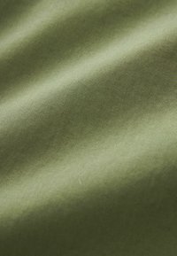 Kangas oliivinvihreä, sileä ja kiiltävä pinta, jossa on hienovarainen poikittaisraidoitus, heijastellen valoa sen pinnalla.