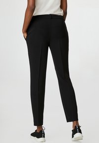 Svarta skräddarsydda byxor med en slät textur, med en åtsittande midja, sidofickor och en rak ben-design. Kambinerat med svarta sneakers.