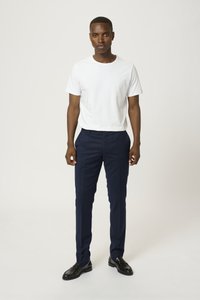 Camiseta blanca de manga corta combinada con pantalones de vestir azul marino y zapatos negros. Los pantalones tienen un corte ajustado y una textura lisa. Diseño simple.