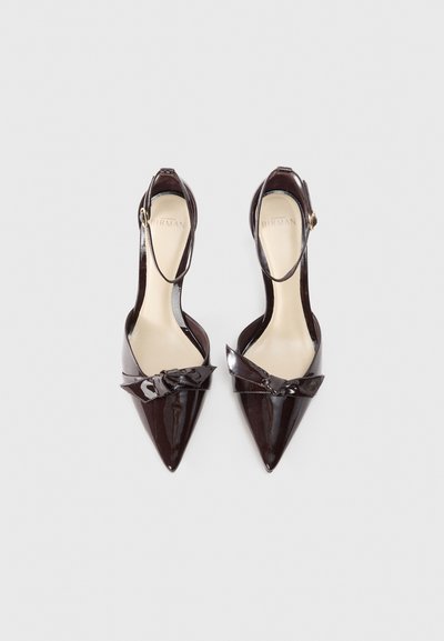 Patent leather pointed-toe shoes in dark brown, featuring an ankle strap and a decorative bow detail across the upper.