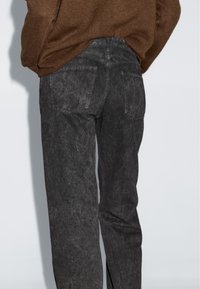 Pantaloni in denim nere con una finitura scolorita, dotati di tasche a toppa e taglio dritto, abbinati a un maglione in maglia marrone.