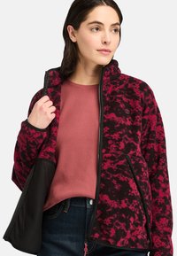 Giacca in pile nera e rosa con colletto alto, chiusura con zip sulla parte anteriore e tasche laterali, caratterizzata da un motivo testurizzato e un orlo in contrasto.
