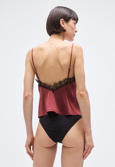 Vīnogu sarkana satīna kamisolē ar mežģīņu apdari gar kakla izgriezumu, regulējamām lencēm un vaļīgu piegriezumu, kombinēta ar melniem augsta griezuma biksītēm.